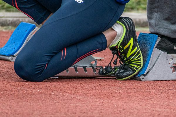 Close-up of a runner's legs ready to start a race, showcasing running shoes and starting block.