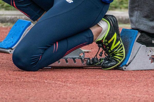 Close-up of a runner's legs ready to start a race, showcasing running shoes and starting block.