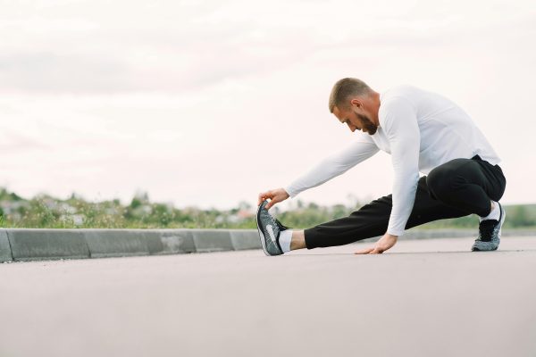 Adult male stretching outdoors, focusing on fitness and healthy lifestyle in a casual sportswear outfit.