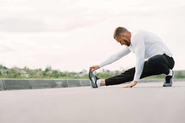 Adult male stretching outdoors, focusing on fitness and healthy lifestyle in a casual sportswear outfit.